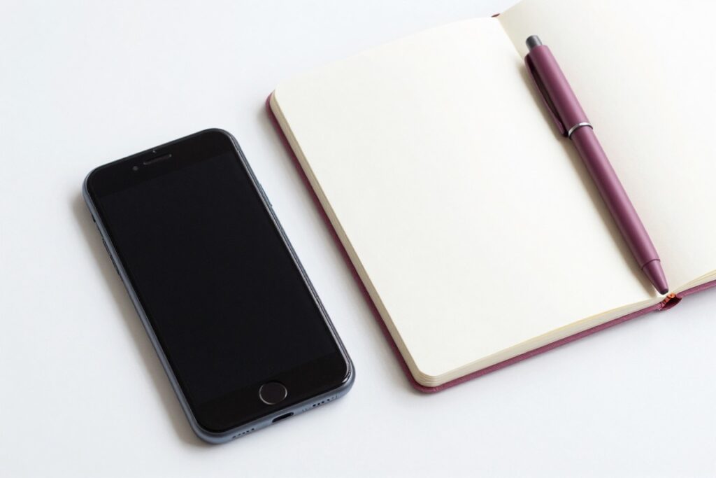 A phone with a blank dark screen beside an open notebook and a mauve pen